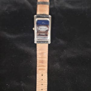 May include: A rectangular Fossil wristwatch featuring a silver-tone metal case and a black leather strap. The back of the watch case is metallic and displays the Fossil logo with the text Authentic Product and the model number VT-2578 clearly visible.