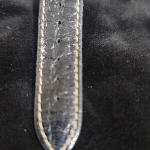 May include: A black watch strap with a textured surface and visible signs of wear. The strap features light-colored stitching along both edges and includes a series of evenly spaced adjustment holes running down the center of the band.