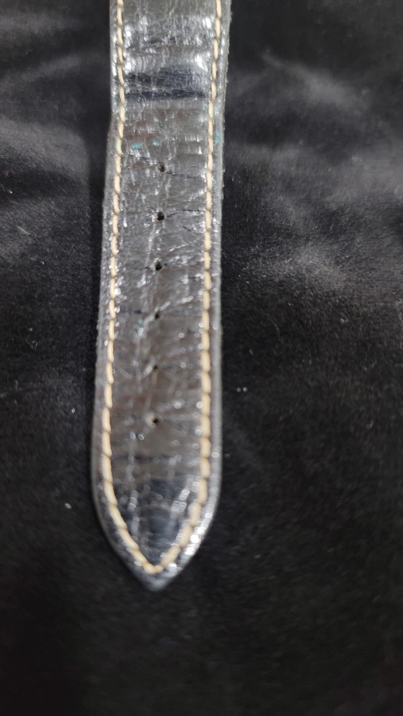 May include: A black watch strap with a textured surface and visible signs of wear. The strap features light-colored stitching along both edges and includes a series of evenly spaced adjustment holes running down the center of the band.