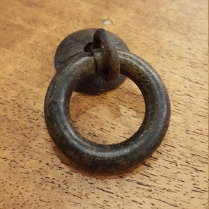 May include: A dark brown metal ring pull cabinet handle with a circular base.