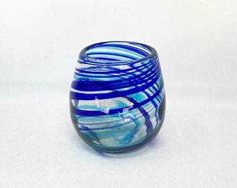 May include: A blue and white glass tumbler with a swirling pattern. The glass is clear with blue and white stripes.