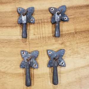 Może przedstawiać: Cztery antyczne metalowe uchwyty do drzwi szafki z wzorem liści i czarnym wykończeniem. Każdy uchwyt ma długi, prosty uchwyt.