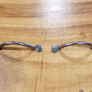 Pode incluir: Duas puxadores de armário de metal prateado com forma curva e um design decorativo nas extremidades.