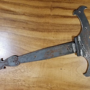 May include: A large, ornate, black metal hinge with decorative flourishes. The hinge is designed for a heavy door or gate.