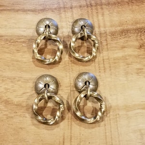 Peut inclure: Quatre boutons de porte en laiton antique avec un anneau torsadé. Chaque bouton a un dessus circulaire décoratif légèrement surélevé.
