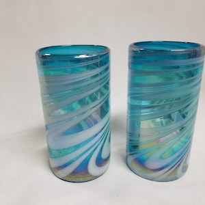 May include: Two blue glass drinking glasses with white swirl designs. The glasses have an iridescent finish.