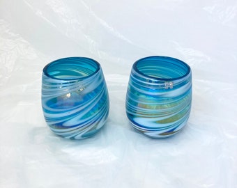 May include: Two blue glass tumblers with white swirling patterns. The glasses have a clear iridescent sheen.