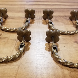 May include: Five antique brass cabinet pulls with a twisted rope design and a four-leaf clover shape at the top.