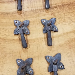 May include: Six black metal drawer pulls with a leaf design. Each pull has a small loop at the top and a long, straight handle.