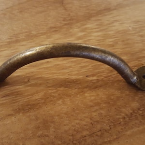 Op de afbeelding: Een rustieke, antieke messing ladegreep met een gebogen handvat en een decoratief, klauwvormig ontwerp aan elk uiteinde.