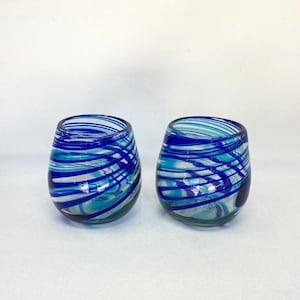 Può includere: Due bicchieri da vino in vetro blu e bianco con motivo a spirale. I bicchieri hanno una base trasparente e sono decorati con spirali blu e bianche.