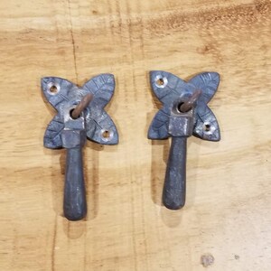 May include: Two black metal cabinet door pulls with a leaf design. The pulls have a simple, rustic style.