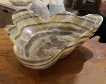 May include: A large, wavy, white and gray onyx bowl with a smooth, polished finish. The bowl is made of natural stone and has a unique, organic shape.