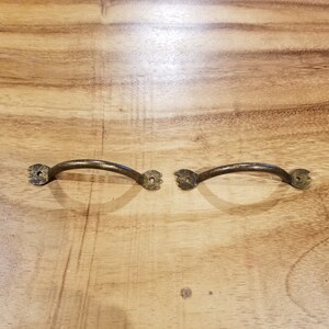 May include: Two antique brass cabinet pulls with a simple curved design. The pulls have a slightly distressed finish.