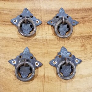 Puede incluir: Cuatro tiradores de cajón de metal de estilo antiguo con diseños ornamentados y tiradores de anillo. Los tiradores son de color plateado y tienen un acabado desgastado.