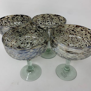Puede incluir: Juego de cuatro vasos de margarita de vidrio transparente con un diseño moteado marrón y blanco. Los vasos tienen una copa ancha y un tallo alto.