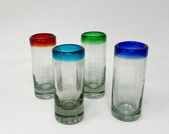 May include: Four clear glass shot glasses with colored rims. The rims are red, blue, green, and blue.