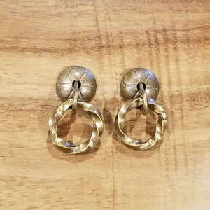 Peut inclure: Une paire de boucles d'oreilles en métal doré avec un anneau torsadé et un dessus décoratif en forme de fleur.