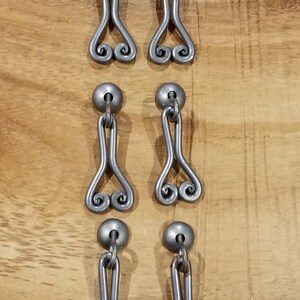 以下が含まれることがあります： ハート型のデザインのシルバーメタル製の引き出しノブ6個セット。各ノブは上部に丸いノブ、下部に装飾的なハート型のループが付いています。