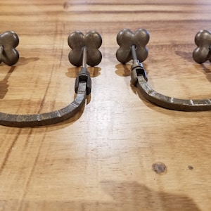 May include: Three antique-style metal drawer pulls with a four-leaf clover design. The pulls are in a U-shape and have a rustic finish.