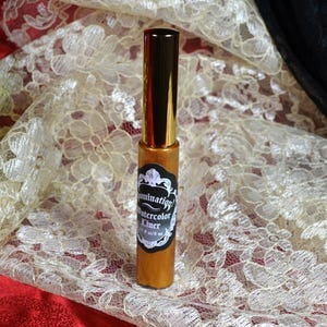 May include: A gold-colored eyeliner with a black and white label that reads "Illumination! Watercolor Liner". The eyeliner has a gold cap and is displayed on a cream-colored lace fabric.