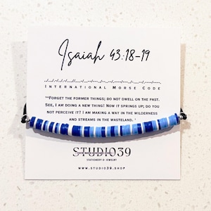 May include: Blue and white beaded bracelet with a black string. The card attached to the bracelet reads "Isaiah 43:18-19" and "INTERNATIONAL MORSE CODE" and includes the scripture verse "'FORGET THE FORMER THINGS; DO NOT DWELL ON THE PAST. SEE, I AM DOING A NEW THING! NOW IT SPRINGS UP; DO YOU NOT PERCEIVE IT? I AM MAKING A WAY IN THE WILDERNESS AND STREAMS IN THE WASTELAND.'" The card also includes the text "STUDIO39" and "STATIONERY & JEWELRY" and "WWW.STUDIO39.SHOP".