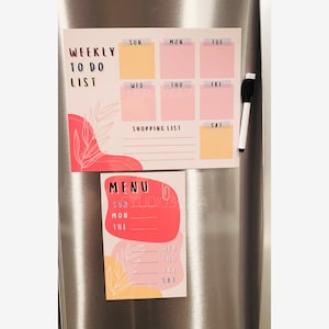 May include: Two pink and yellow magnetic dry-erase boards with a weekly to-do list, shopping list, and menu planner. The boards are on a silver refrigerator.
