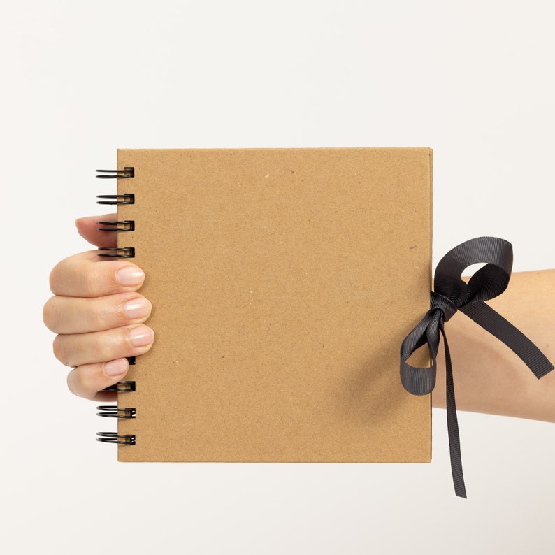 May include: A brown notebook with a black ribbon tied around it. The notebook is held in a hand.