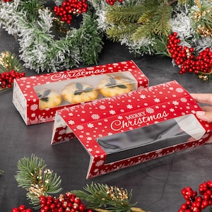 May include: Red and white Christmas-themed bakery boxes with clear windows to display the baked goods inside. The boxes have a snowflake pattern and the text "Merry Christmas".
