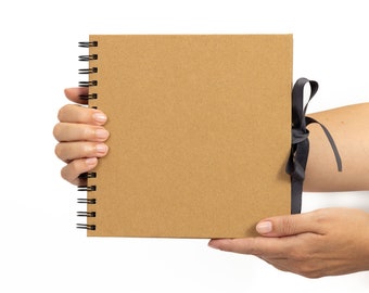 May include: A brown cardboard spiral bound notebook with a black ribbon tied around it.