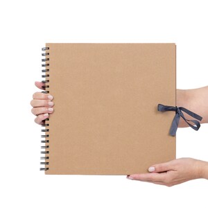 May include: A brown cardboard scrapbook with a black spiral binding and a black ribbon tied around it.