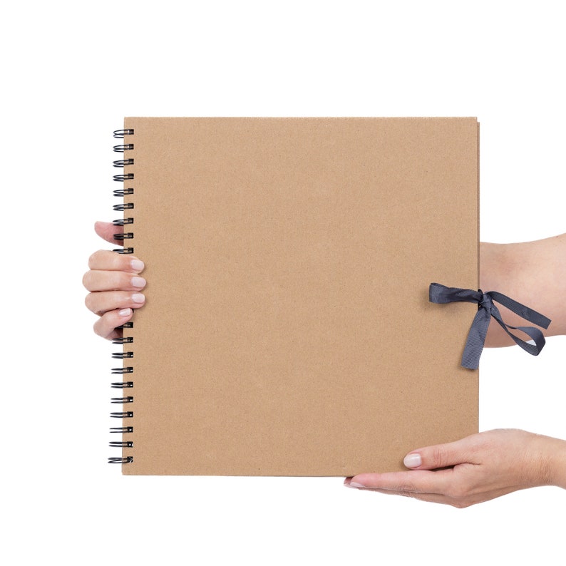 May include: A brown cardboard scrapbook with a black spiral binding and a black ribbon tied around it.