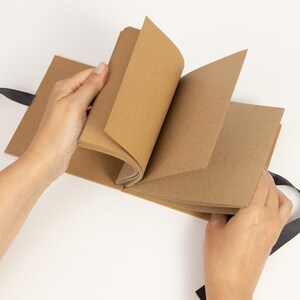 May include: A brown paper scrapbook with black ribbon ties. The scrapbook is open to reveal blank pages.