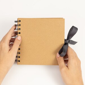 May include: A brown spiral bound notebook with a black ribbon tied around it.
