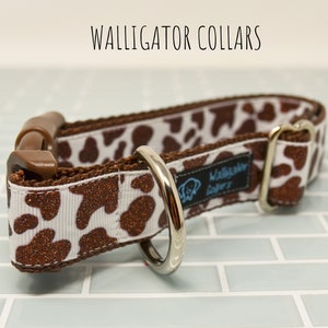 May include: A brown and white dog collar with a cow print pattern and glitter accents. The collar has a brown plastic buckle and a silver metal D-ring. The collar is labeled "Walligator Collars".