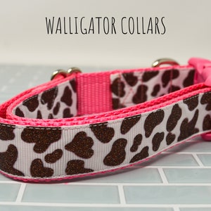 May include: A pink and white dog collar with a brown cow print pattern. The collar has a pink buckle and silver hardware. The text "WALLIGATOR COLLARS" is visible at the top of the image.