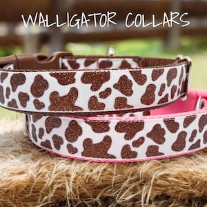 May include: Two dog collars with a brown and white cow print pattern. The top collar is brown with a pink accent. The bottom collar is pink with a brown accent. The collars are made of fabric with a glitter finish. The text "WALLIGATOR COLLARS" is visible at the top of the image.