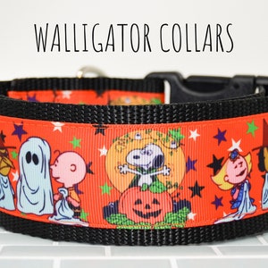 Puede incluir: Un collar de perro negro con una cinta roja y blanca con un patr&oacute;n de personajes de Peanuts vestidos con disfraces de Halloween. La cinta tiene un patr&oacute;n repetitivo de estrellas, calabazas y fantasmas. El texto "WALLIGATOR COLLARS" es visible sobre el collar.