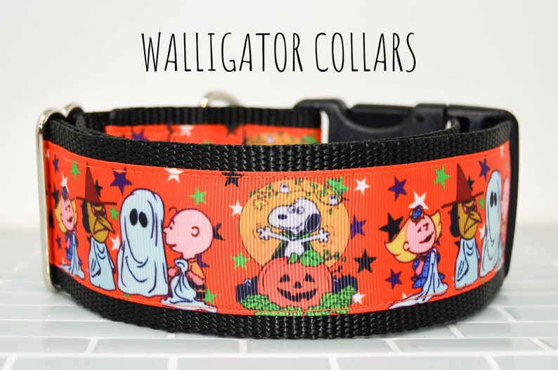 Puede incluir: Un collar de perro negro con una cinta roja y blanca con un patr&oacute;n de personajes de Peanuts vestidos con disfraces de Halloween. La cinta tiene un patr&oacute;n repetitivo de estrellas, calabazas y fantasmas. El texto "WALLIGATOR COLLARS" es visible sobre el collar.
