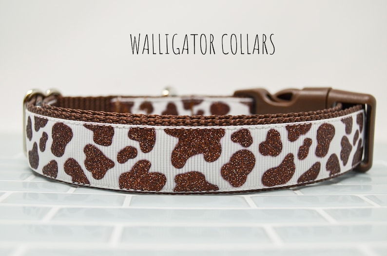 May include: A white and brown dog collar with a brown glitter cow print pattern. The collar has a brown plastic buckle.