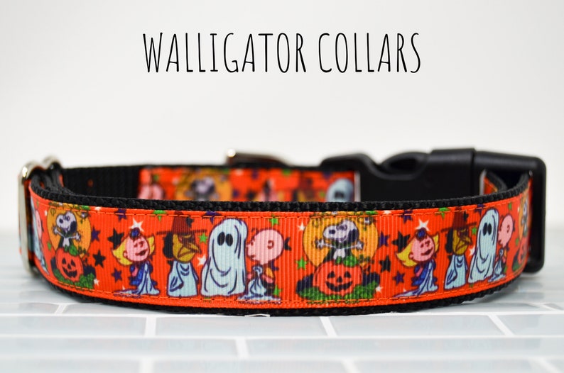 Puede incluir: Un collar de perro rojo y negro con un estampado de tem&aacute;tica de Halloween con personajes de Peanuts como Snoopy, Charlie Brown y Lucy. El collar tiene una hebilla negra y un anillo en D plateado.
