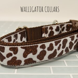 May include: A brown and white dog collar with a cow print pattern and brown glitter accents. The collar has a silver buckle and a brown plastic slider.