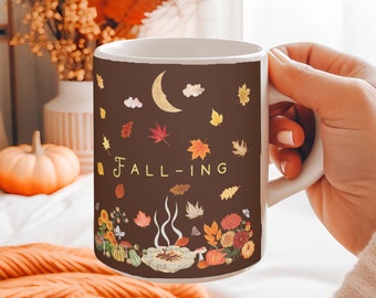 May include: A brown ceramic mug with a white rim and handle. The mug features a fall-themed design with a crescent moon, leaves, and the text "FALL-ING".