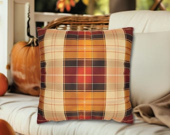 May include: A plaid throw pillow with a red, orange, yellow, and black pattern. The pillow is on a white couch with a brown blanket.