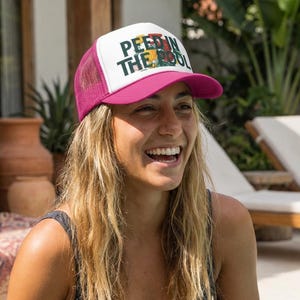 Puede incluir: Gorra de camionero magenta y blanca con el texto "PEE IN THE POOL" en verde y amarillo. La gorra tiene una parte trasera de malla y una visera curva. La gorra la lleva una persona.
