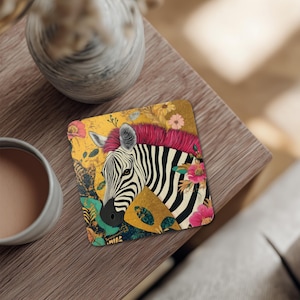 May include: Square coaster featuring a zebra with a pink mohawk and floral accents. The zebra is set against a gold background with colorful flowers. The coaster is on a wooden table.