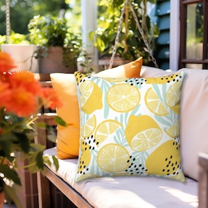 Puede incluir: Una almohada blanca con estampado de limón. La almohada presenta limones amarillos, hojas verdes y puntos negros sobre un fondo blanco.
