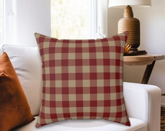 May include: A red and beige checkered throw pillow with a white background. The pillow is sitting on a white couch.