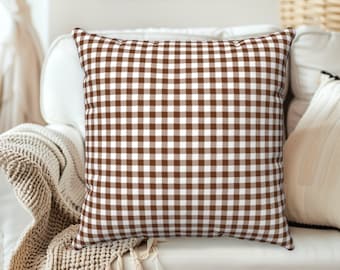 Puede incluir: Una almohada de tiro de cuadros marrones y blancos con un patrón cuadrado. La almohada está en un sofá blanco.