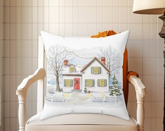 Può includere: Cuscino bianco con un'illustrazione ad acquerello di una casa bianca con una porta rossa e persiane verdi, circondata da alberi e una recinzione, con luci a stringa appese sopra.
